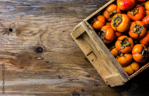 Box of fresh fruits persimmon kaki on wooden background. Copy space photo