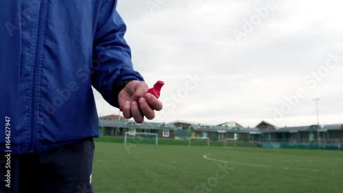 coach holds red whistle in his hand