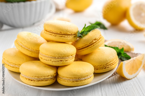Plate with tasty lemon macarons on white wooden table, closeup
