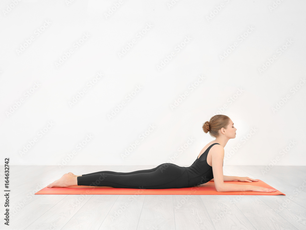 Fototapeta premium Young beautiful woman practicing yoga pose near white wall indoors