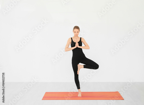 Young beautiful woman practicing yoga pose near white wall indoors