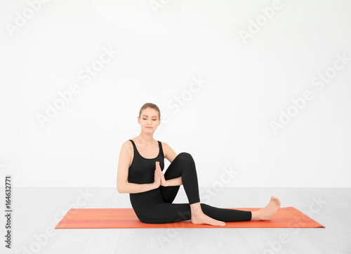 Young beautiful woman practicing yoga pose near white wall indoors