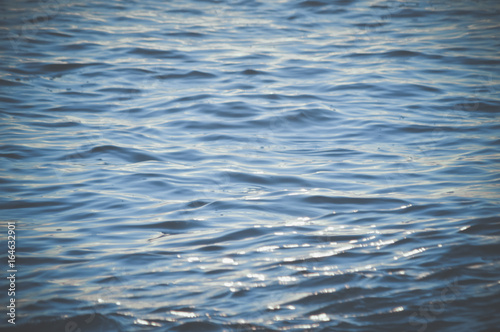 Blurry light on the water textured background. Sunny outdoors seascape bright surface