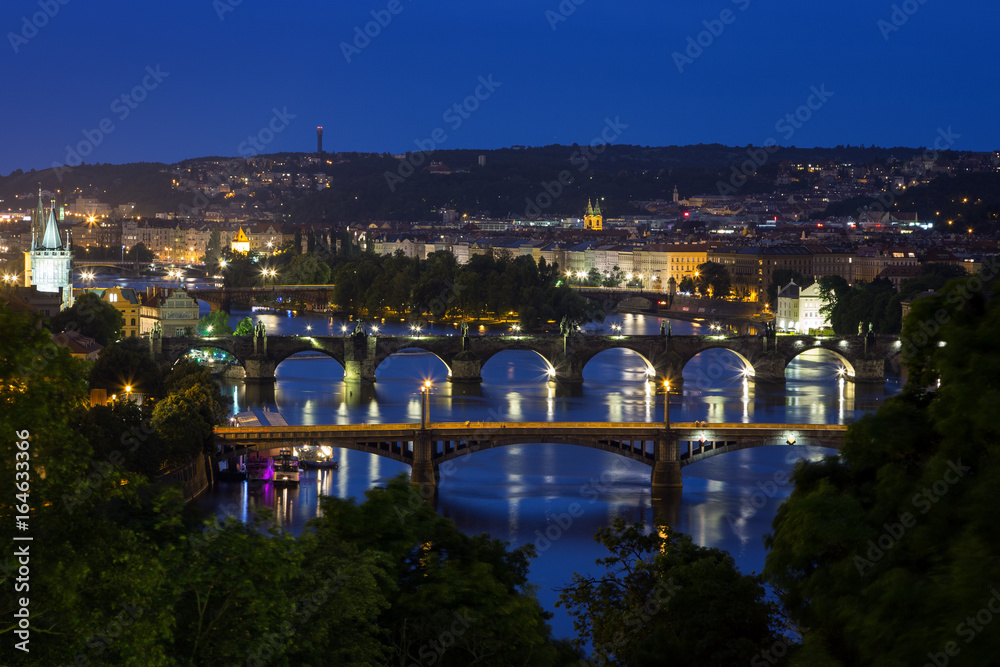 Lit buildings and bridges over Vltava River in Prague, Czech Republic, viewed slightly from above at night.