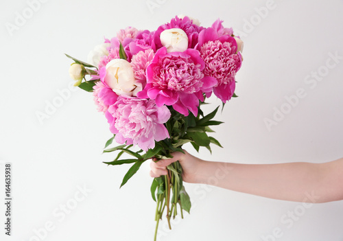 Female hand holding beautiful bouquet with fragrant peonies on light background