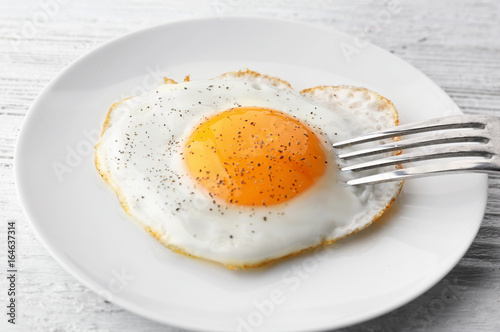 Plate with sunny side up fried egg on wooden table