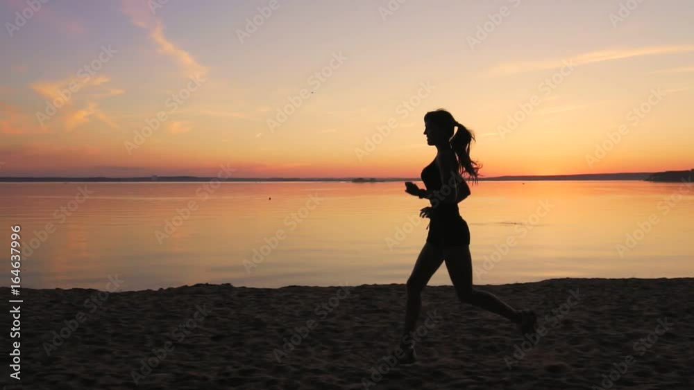 Young athlete runner is runing along the shore of the lake at sunset