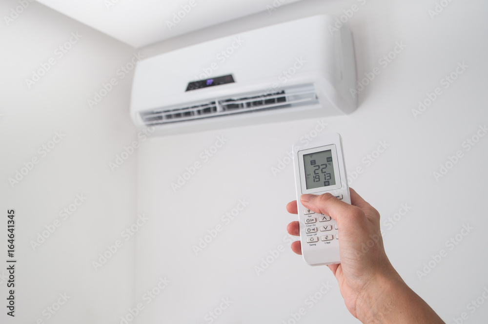 Hand holding remote control, adjusting temperature of air conditioner mounted on a white wall. Indooor comfort temperature Hand holding remote control, adjusting temperature of air conditioner mounted on a white wall. Indooor comfort temperature