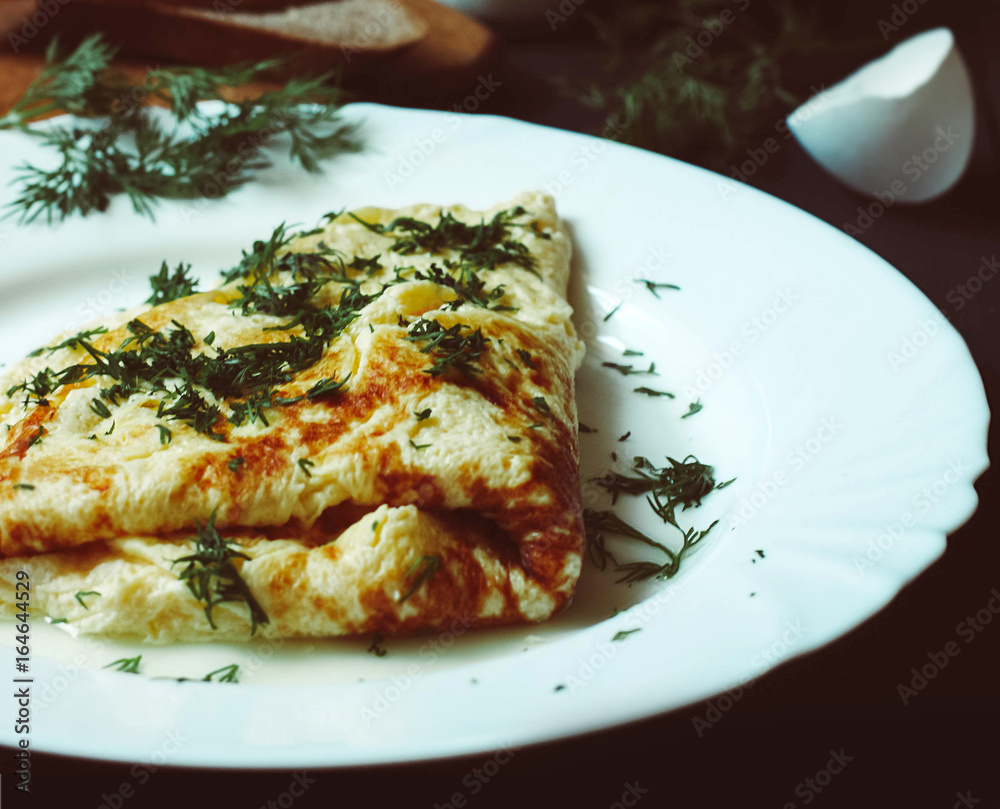 Tasty omelette with greens on a white plate, bread and chicken eggs on a dark wooden background Tasty omelette with greens on a white plate, bread and chicken eggs on a dark wooden background