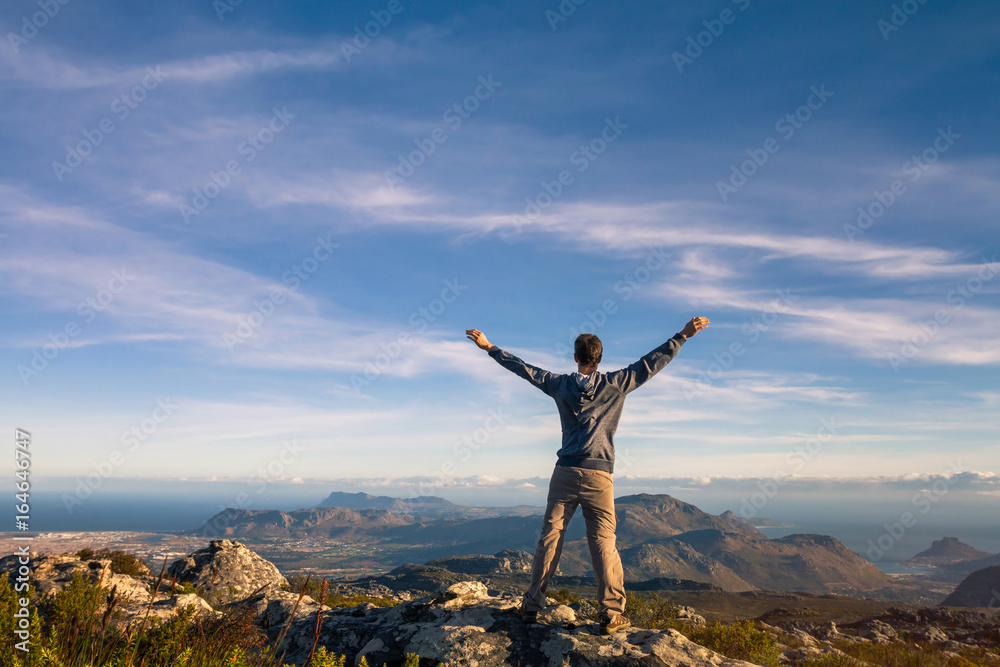 man standing with raised hands on top of Table mountain in Cape Town, South Africa