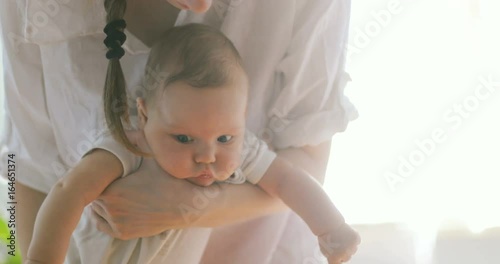 Mother rocking baby lull swinging dandle boy newborn child kid carrying entertain white gentle home sunny peeking calm quiet big eyes cheeks amuseing amuse curious swing cute nice girl thoughtful hug