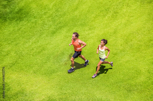 Runners running healthy people lifestyle. Active couple jogging together on grass park view from above. Summer weight loss training program.