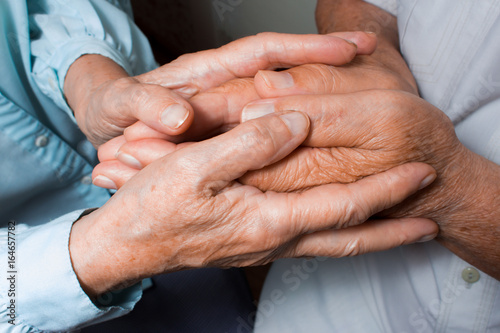 Hands of two loving senior people on a dark background