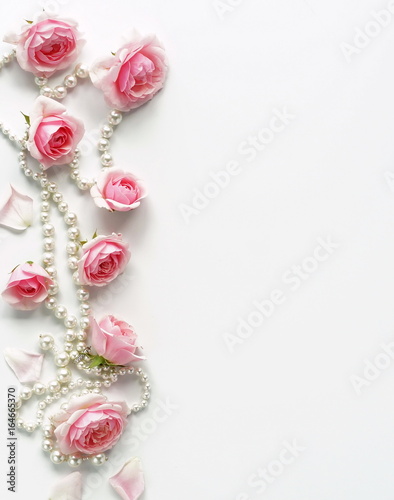 A frame of pink roses and beads on a white background.Top view. Copy space