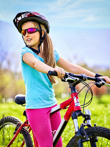 Child traveling bicycle in summer park. Children road bike for running on green grass aganist sky blue. Cycling trip is good for health. Kid travels unaccompanied. Sports program against obesity.