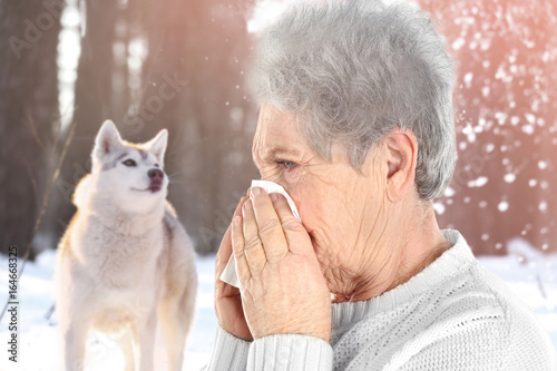 Senior ill woman with tissue and pet on background. Concept of allergies to dogs