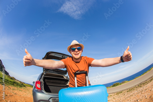 Summer, car, trip and vacation concept - Happy traveler sitting in car open trunk and showing thumbs up.