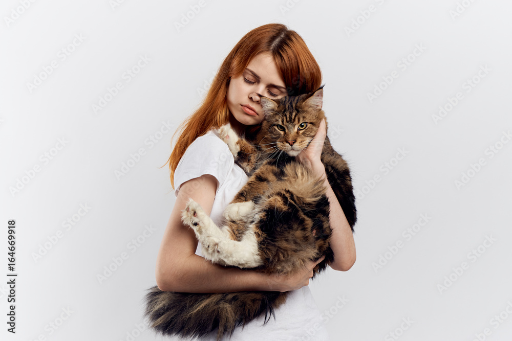 Beautiful young woman on a light background holds a cat