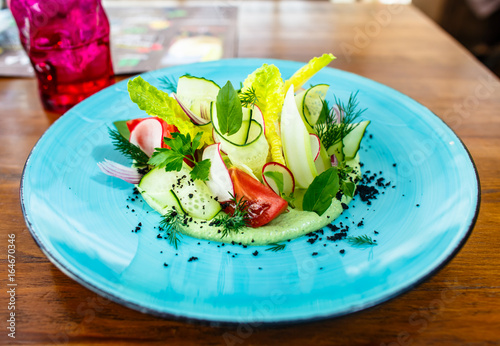 Vegetable salad of cucumbers, tomatoes, radish and celery on a blue plate.