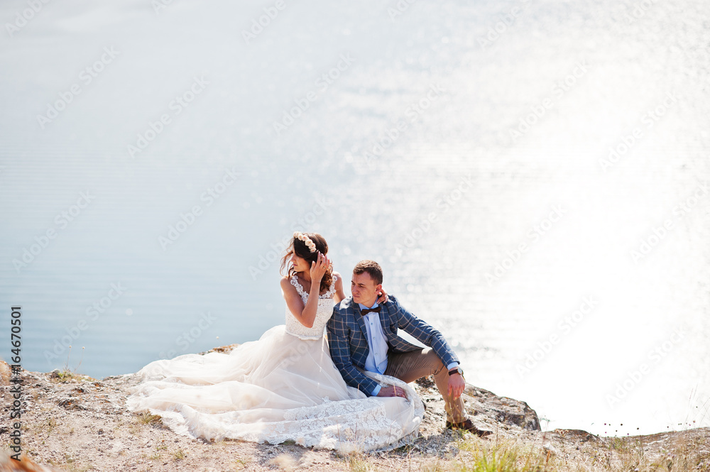 Stunning young wedding couple sitting on the edge of the cliff with a beautiful scenery on the background.