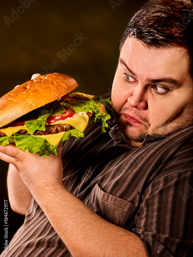 Man eating fast food hamberger. Fat person with brutal look made great huge hamburger and admires him, intending to eat it. Junk meal leads to obesity. Person regularly overeats concept .