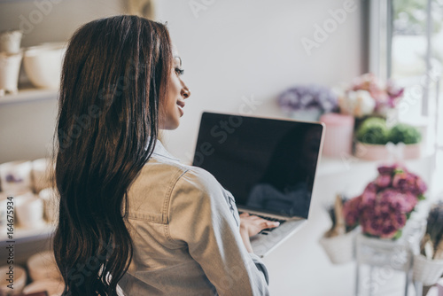 smiling young african american woman using laptop with blank screen while working in flower shop