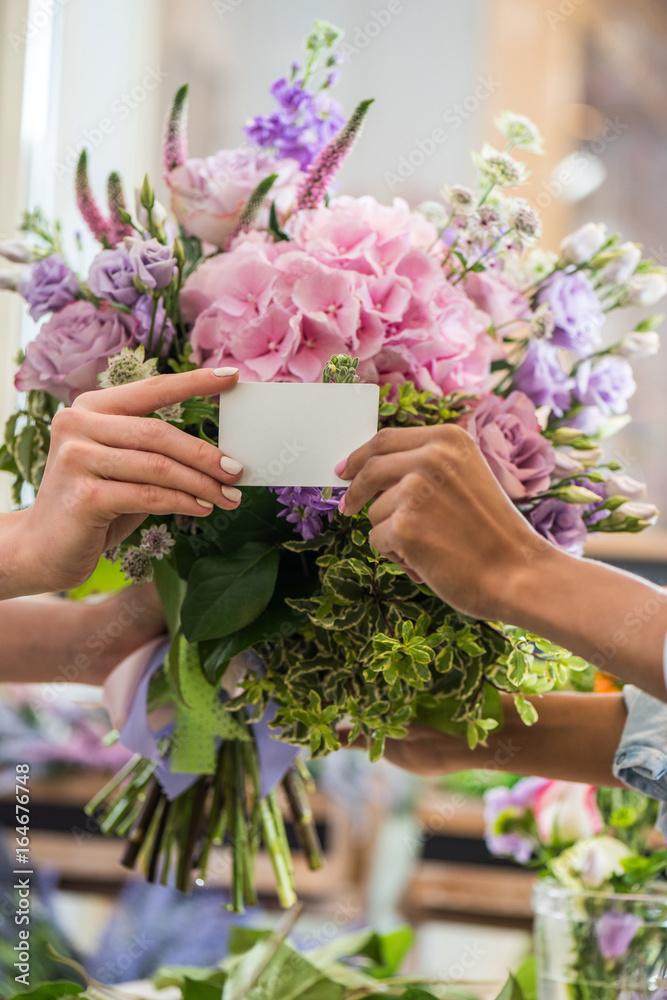 Φωτογραφία close-up partial view of female hands holding blank business card and bouquet of
