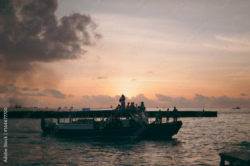 The boat with people in the ocean at sunset