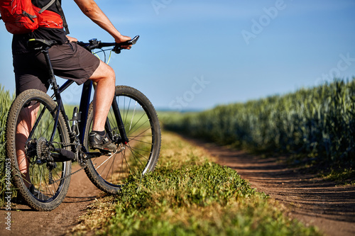 Fototapeta Naklejka Na Ścianę i Meble -  Attractive one cyclist on mountainbike on path near green fields in the countryside in the summer season.