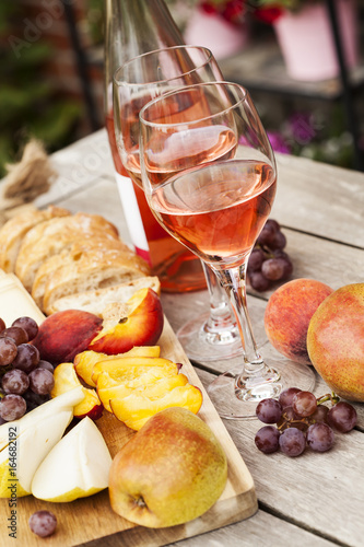 Canvas Print Two glasses of rose wine and board with fruits, bread and cheese on wooden table