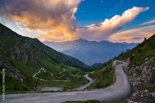 Dirt mountain road leading to high mountain pass in Italy (Colle delle Finestre). Expasive view at sunset, colorful dramatic sky, adventures in summer time, Italian Alps. photo