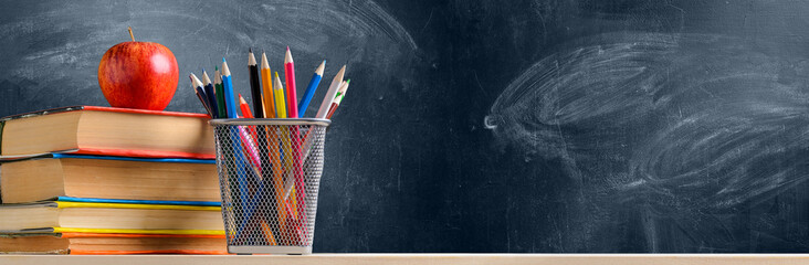 Back to School. Accessories, books and fresh apple against chalkboard
