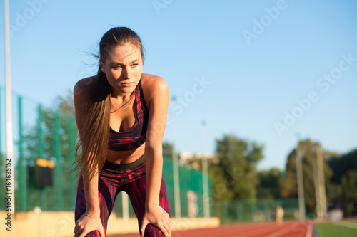 Young woman standing bent over and catching her breath during a running session