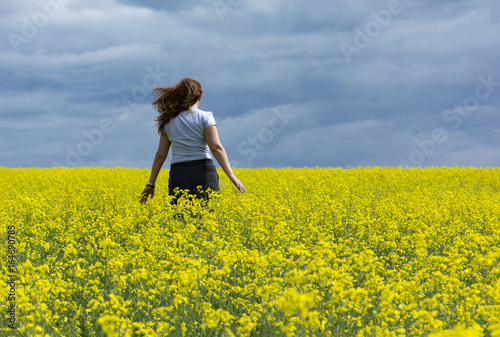 girl one, 1 runs in a field of yellow rapeseed against the blue sky © Elena