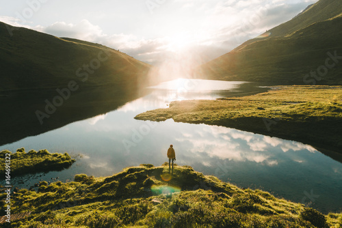 Young male standing in front of a warm summer sunrise reflection of the sky at a mountain lake.