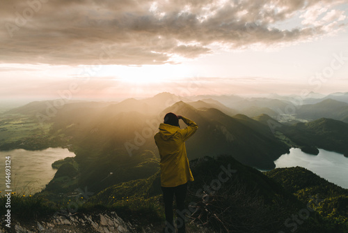 Male photographer in yellow jacket looking over a valley with mountains, forest and lake in Germany in the morning photo