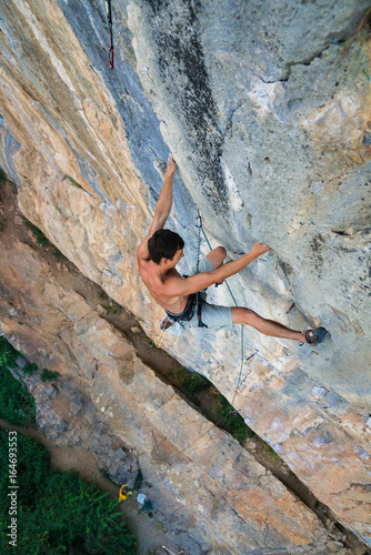 sports man climbs an overhang rock near forest