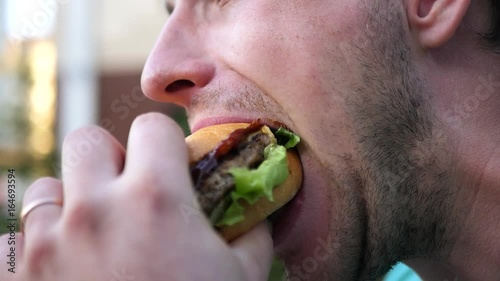 An adult man with a beard bites off a delicious juicy hamburger, smeared his face with ketchup. SLOW MOTION. HD, 1920x1080.