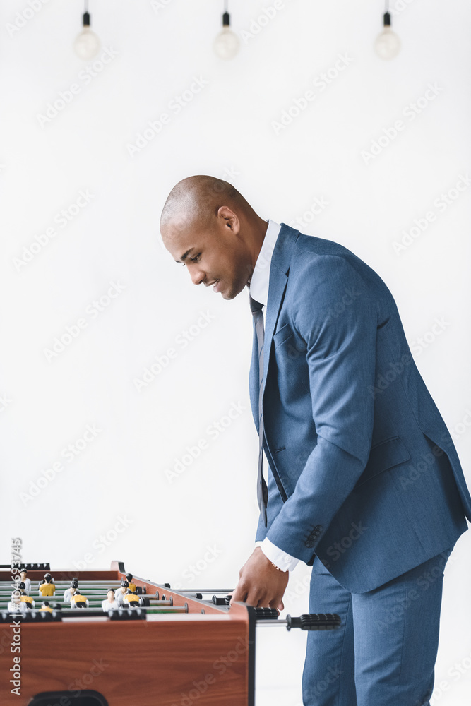 side view of focused businessman in suit playing table football side view of focused businessman in suit playing table football