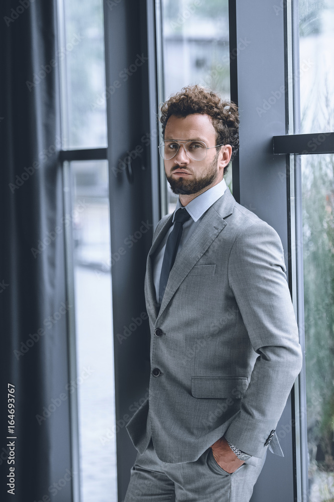 confident businessman in suit with hands in pockets looking at camera confident businessman in suit with hands in pockets looking at camera