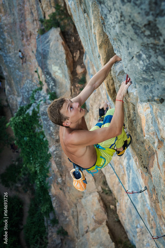 sportsman Dmitrii Fakirianov climbs an overhang rock and grips the hold