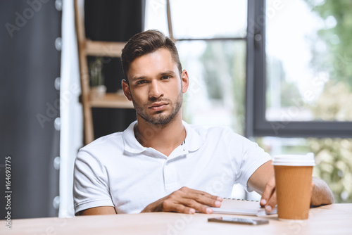 portrait of confident caucasian businessman looking at camera while sitting at workplace in office