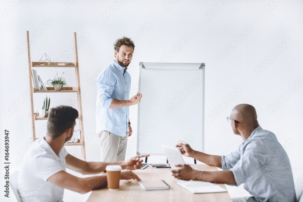 Obraz premium young businessman at white board making presentation to colleagues