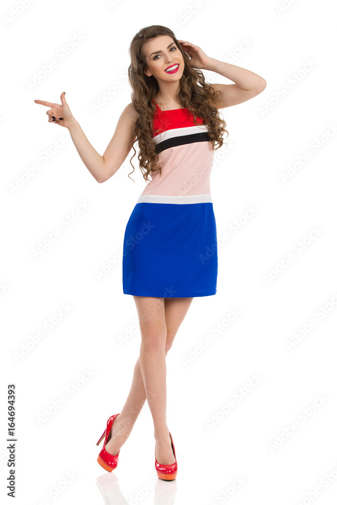 Young Woman In Mini Dress And High Heels Is Smiling And Pointing Young Woman In Mini Dress And High Heels Is Smiling And Pointing