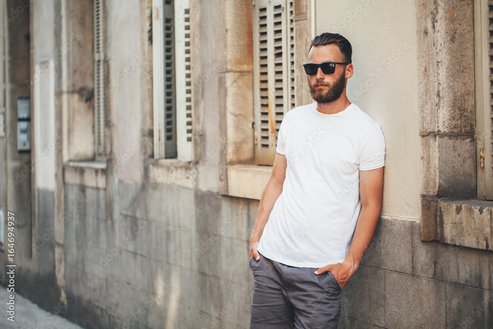 Hipster handsome male model with beard wearing white blank t-shirt with space for your logo or design in casual urban style Hipster handsome male model with beard wearing white blank t-shirt with space for your logo or design in casual urban style