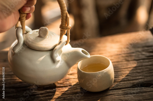 фотографія Tea pot  and cup of tea on wood table under morning light , soft focus