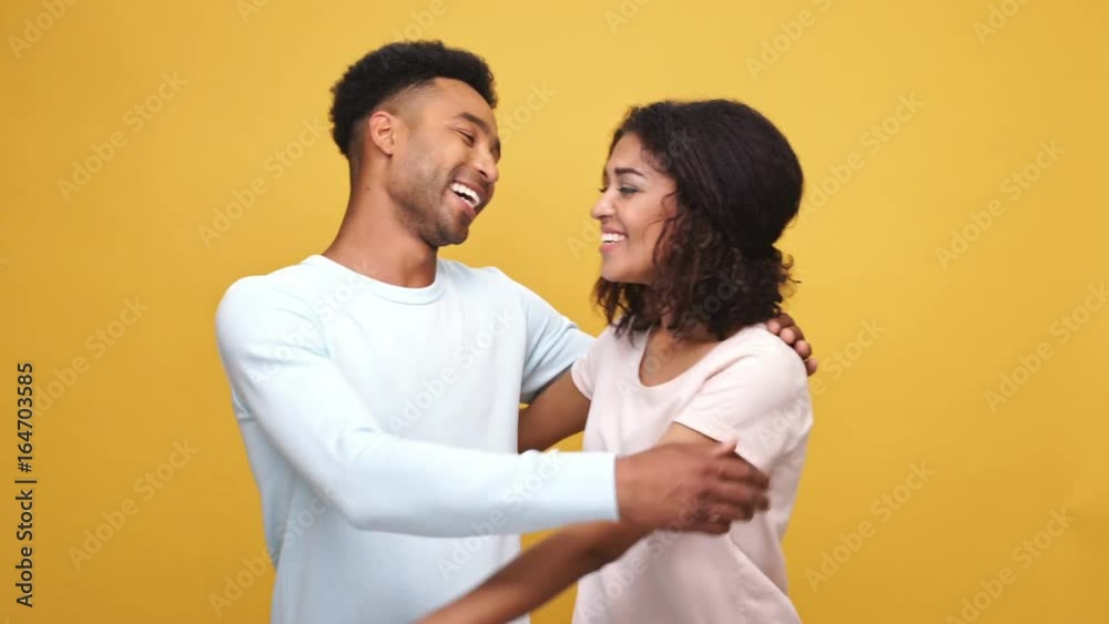 Smiling young afro american couple hugging and laughing isolated over yellow background