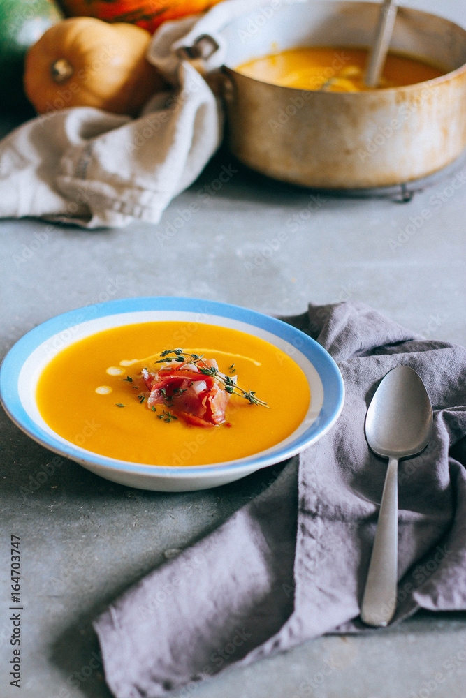 A plate of pumpkin soup, with prosciutto and thyme, on a gray background A plate of pumpkin soup, with prosciutto and thyme, on a gray background