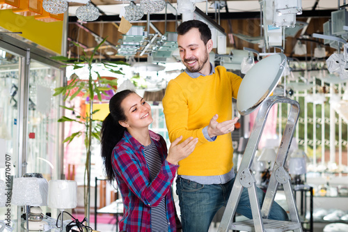 Young man and girl are choosing stylish round matt glass ceiling lamp.