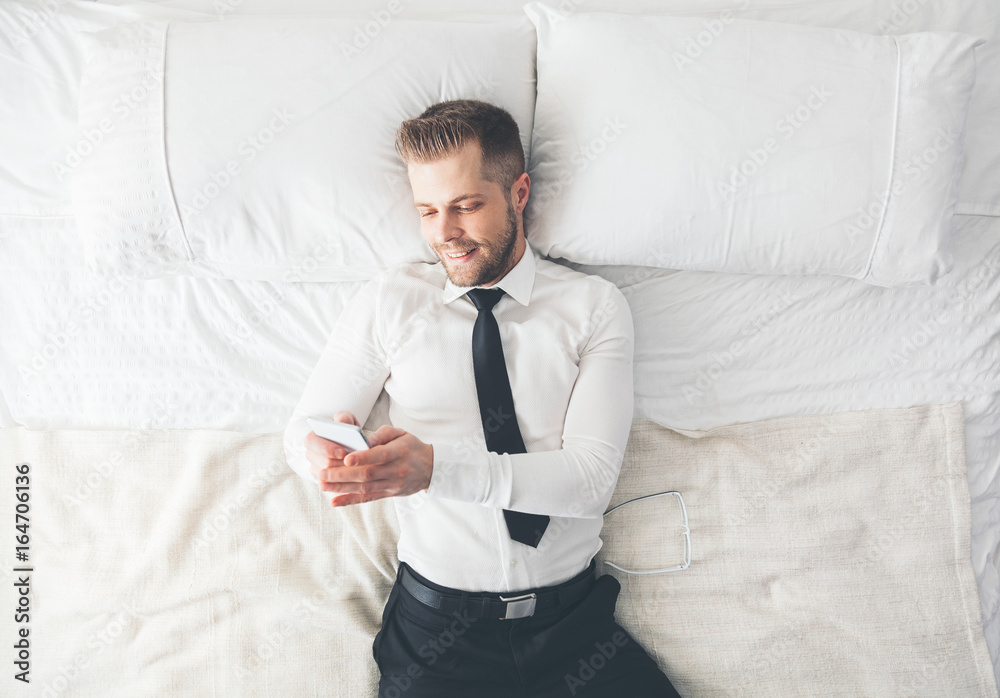 Top view. Handsome businessman lying on bed texting from his smartphone Top view. Handsome businessman lying on bed texting from his smartphone